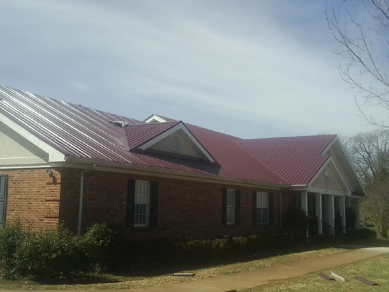 Red metal roof with gabled entries on a long brick building, from a Hail Damage Roof Repair job in Manns Choice