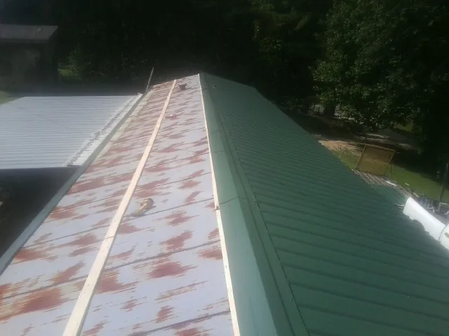 Old rusted panels beside newly installed green metal roofing — Wind Damage Roof Repair by Roofing Brothers in Manns Choice