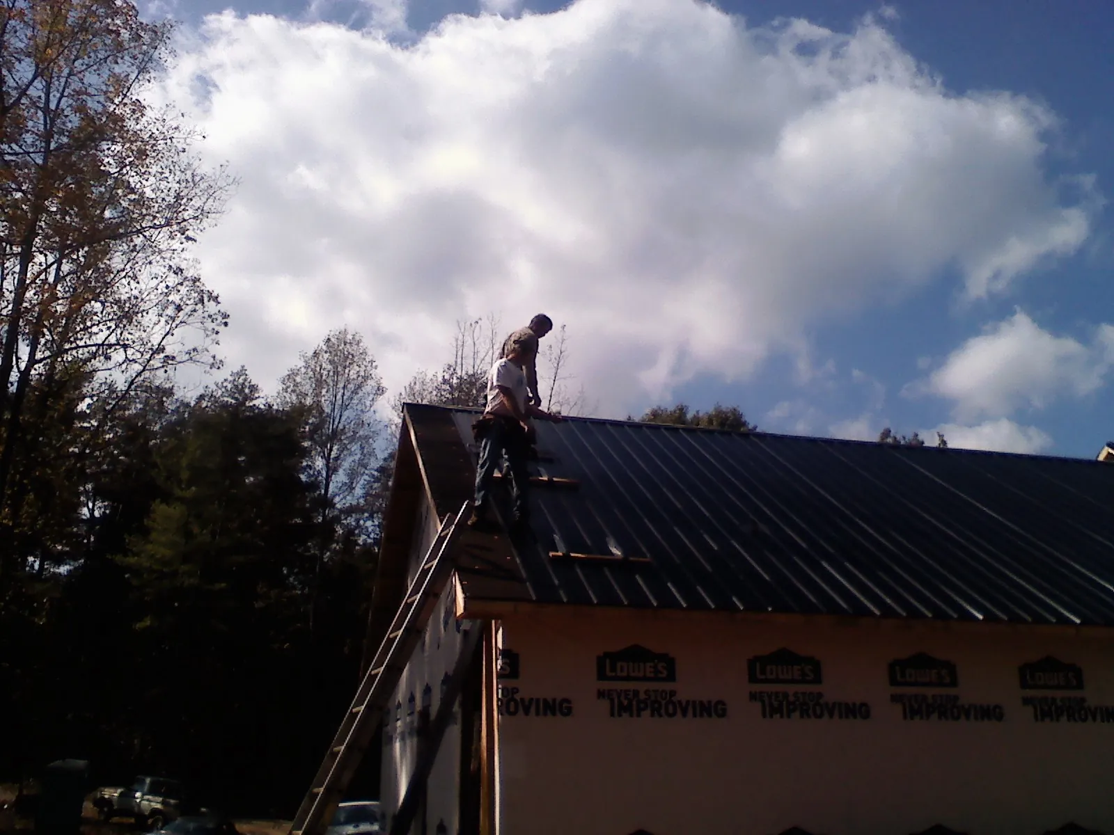 Roofer fastening dark metal panels high against a cloudy sky, from a Roof Inspection job in Manns Choice