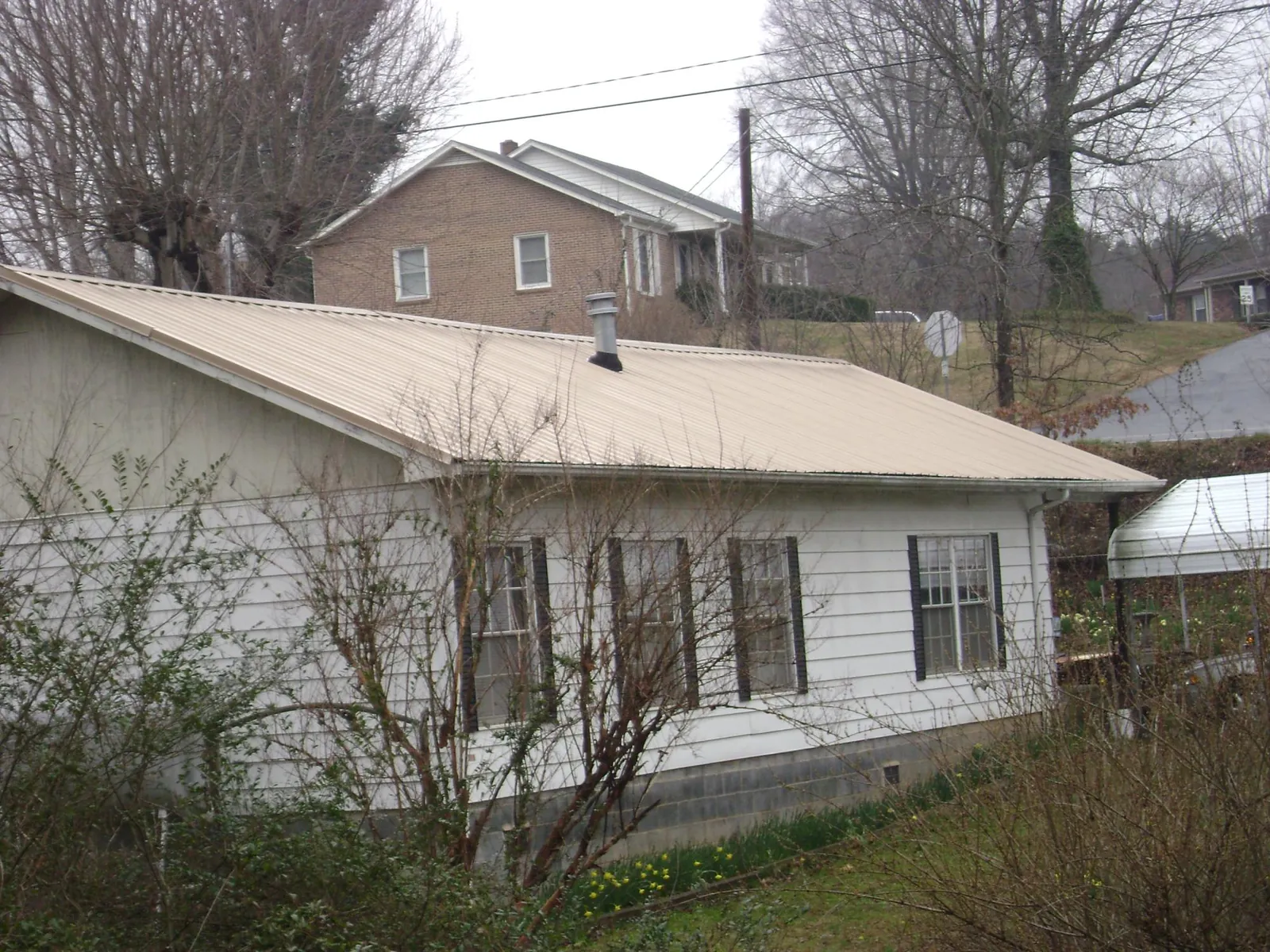 Tan metal roof on a white sided house set into a hillside — Commercial Roofing by Roofing Brothers in Manns Choice